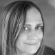 A black and white photo of photographer MIchelle Gabel, who is looking into the camera with a hint of a smile. She has blonde hair and is wearing a black t-shirt.